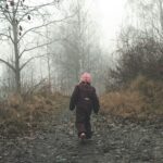 dziecko w czarnym kombinezonie idzie leśną ścieżką