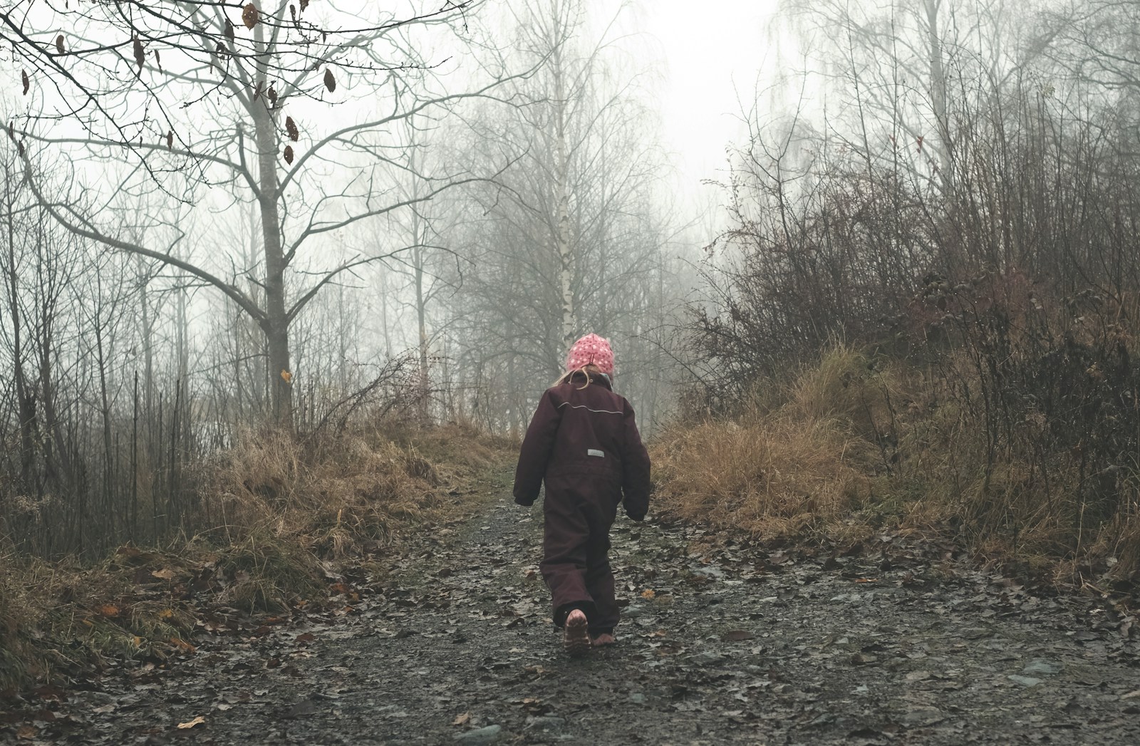 dziecko w czarnym kombinezonie idzie leśną ścieżką
